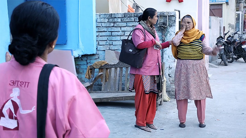 Two female ASHAs measure a lady's visual acuity in the community