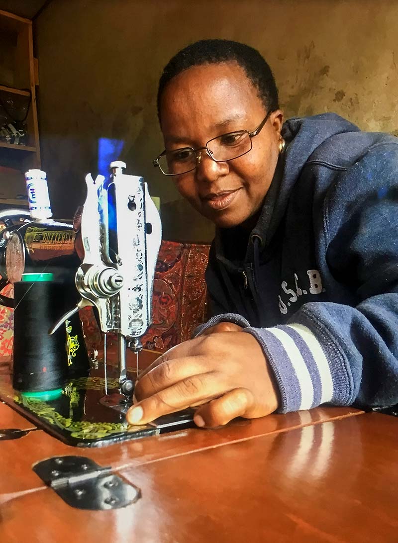 A lady who is wearing spectacles threads the needle on her sewing machine