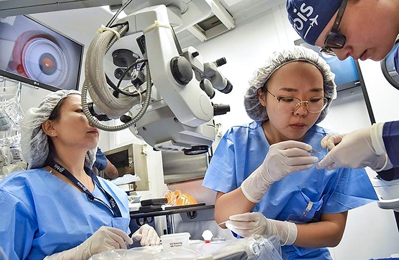 Three staff in a operating theatre using an operating microscope