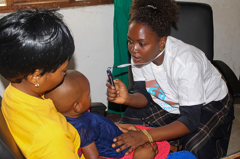 A female eye health worker uses an Arclight to examine the eyes of a child who is siting on his/her mother's knee