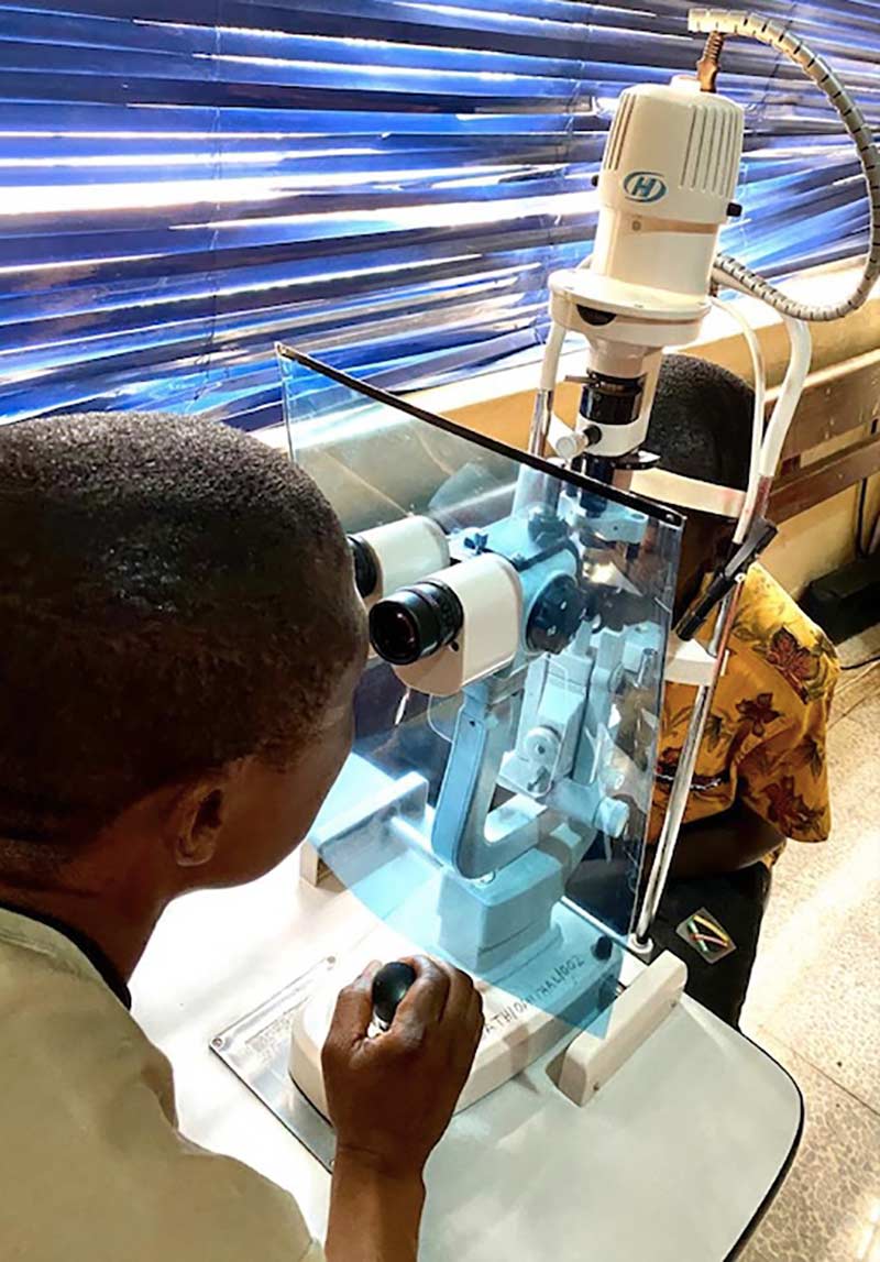 An ophthalmologist examines a patient's eye with a slit-lamp to which has been attached a perspex shield