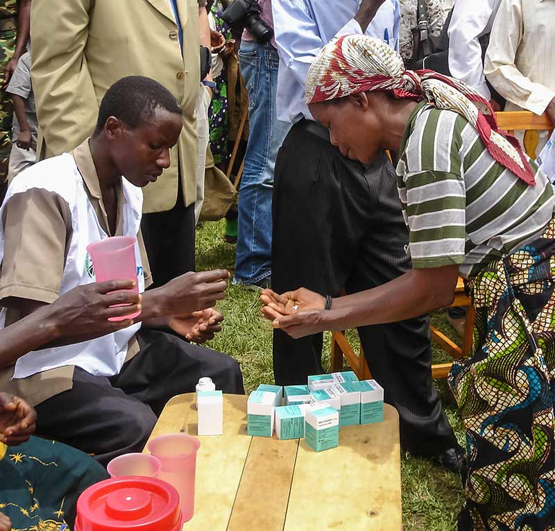 African male ivermectin administrator counting out tablets for an African lady.