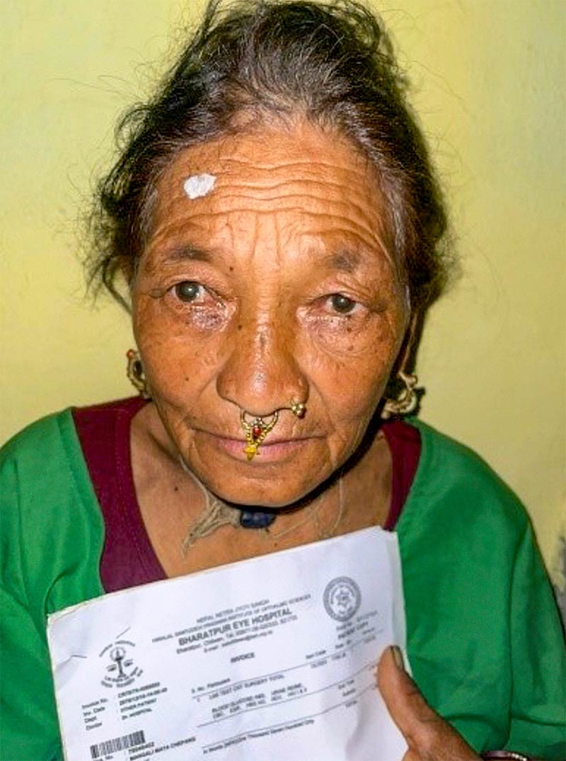 A female nepalese cataract patient holding her patient forms. She has a white spot painted on her forehead above her right eye.