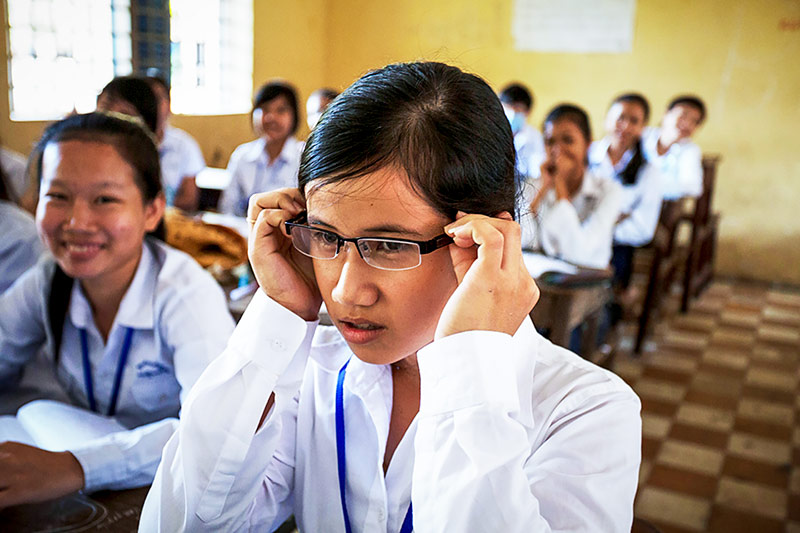 Girl putting spectacles on spectacles on while sitting in the classroom