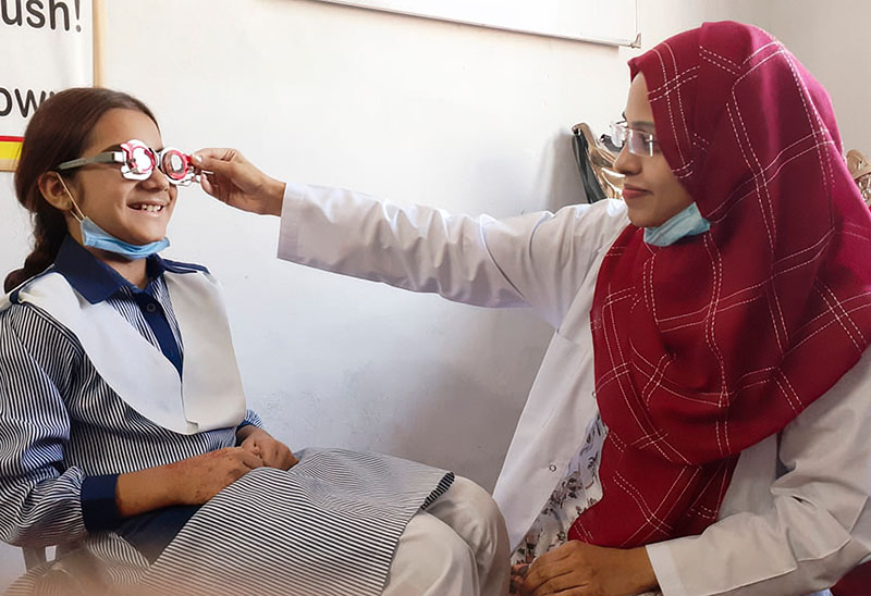 A female eye care worker holds a trial frame up against the eyes of a young girl