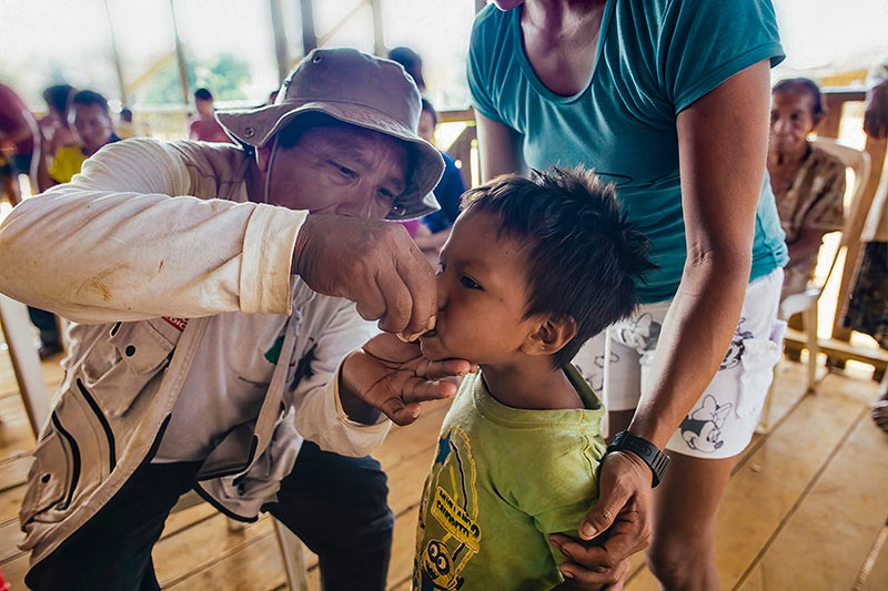 A male health worker gives azithromycin to a small child who is accompanied by his mother.