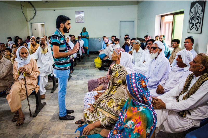 A male health worker talks to a waiting room full of patients